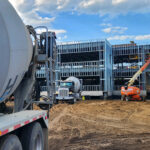 A construction site with a cement truck, partially built metal framework, and a cherry picker.
